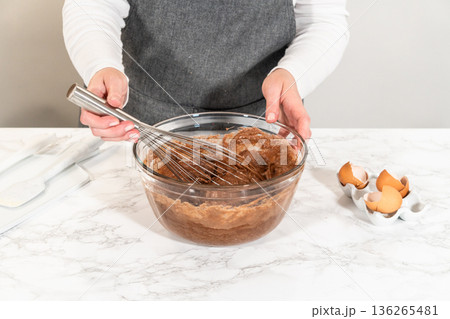 With a hand whisk, the ingredients are expertly mixed in a glass mixing bowl - creating this delectable Chocolate Bundt Cake. 136265481