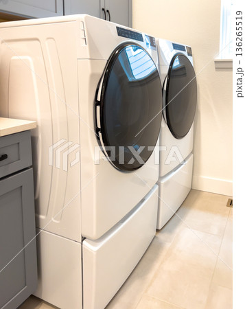 A laundry room includes a front loading washer and dryer set with a built in gray cabinet. The space is modern, functional, and clean in design. A laundry room includes a front loading washer and dryer set with a built in gray cabinet. The space is modern, functional, and clean in design. 136265519