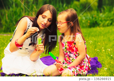 Mother and child blowing soap bubbles outdoor. Mother and child blowing soap bubbles outdoor. 136266915