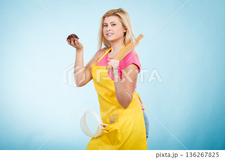 Woman holding cupcake, rolling pin, colander wearing apron 136267825