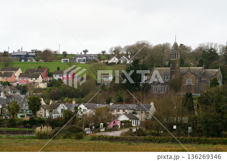 Village houses and old church building nestled in the green hills of rural Ireland on a cloudy day. 136269346
