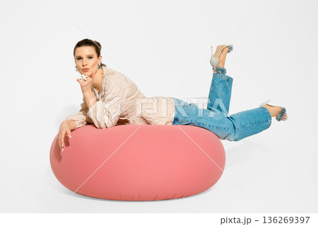 Model poses on pink bean bag while wearing casual clothes and high heels in studio setting 136269397
