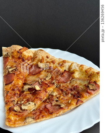A close-up shot of a large classic pizza with cheese, ham, and mushrooms. A delicious, nutritious, and quick meal. 136269456