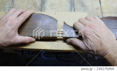 The carpenter joins two sawn wooden parts from a piece of furniture decor by gluing dowels inserted into the holes; he connects the fragments for gluing using dowels and wood glue on the workbench 136270068