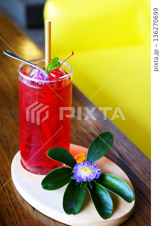 A glass of red soda with a cherry and violet flower decorated on topping on wooden table 136270699
