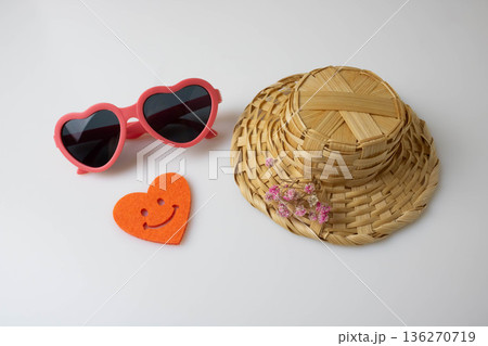 Children's heart-shaped sunglasses, a straw hat, and an orange felt heart on a light background. Summer vacation concept 136270719