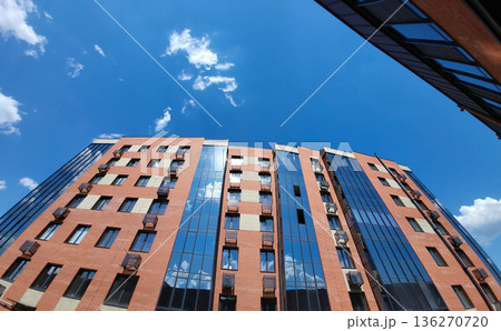 The blue sky with clouds is reflected in the glass facade of the house 136270720
