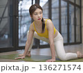 Woman in a yellow top and white pants is doing a yoga pose on a green mat 136271574