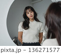 Woman is standing in front of a mirror, wearing a white shirt and black pants 136271577