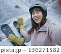 Woman wearing a helmet and a pink jacket is posing with her snowboard 136271582