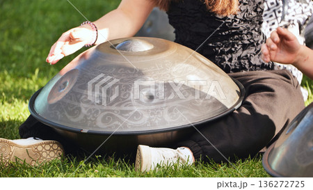 Musician playing hang drum with intricate arabic calligraphy outdoors on green grass 136272725