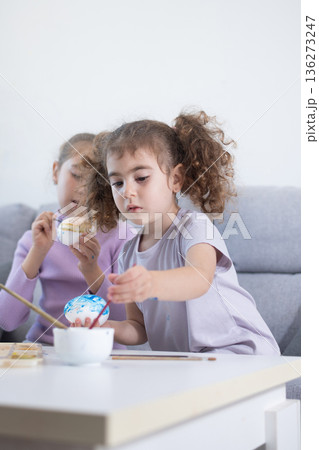 Two sisters decorating Easter eggs. 136273247