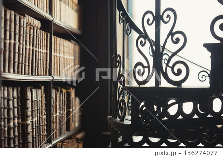 Interior of historic library with bookshelves and wrought iron staircase 136274077
