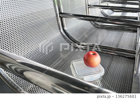 healthy snack on the go with red apple and glass lunch box on perforated metal bench at transit station 136275681