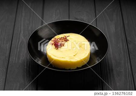 Creamy mashed potatoes puree with microgreens garnish on black plate, dark wooden background 136276102