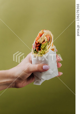 Hand holding grilled salmon wrap with avocado sauce on green background 136276368
