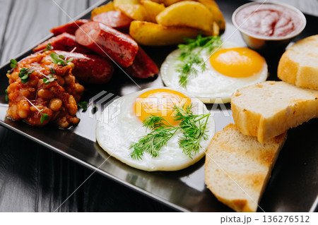 Breakfast plate with fried eggs, sausage, potato wedges and bread, top view 136276512