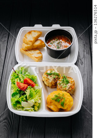 Takeaway lunch box with tomato soup, salad and cutlets on dark wooden table 136276514