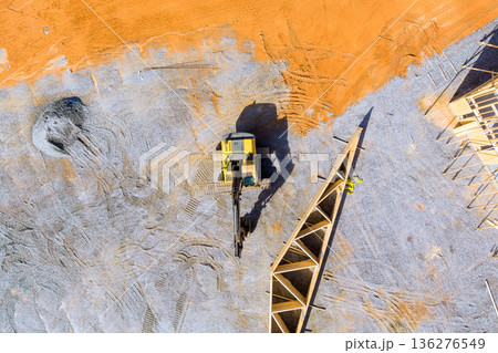 Crane machine lifting into joins wooden trusses frame while workers handle building materials on construction site. 136276549