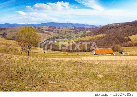 rural landscape with village in valley. outdoor adventures in countryside with rolling hills and snowy mountains in early spring. green environment sustainability and protection background rural landscape with village in valley. outdoor adventures in countryside with rolling hills and snowy mountains in early spring. green environment sustainability and protection background 136276855