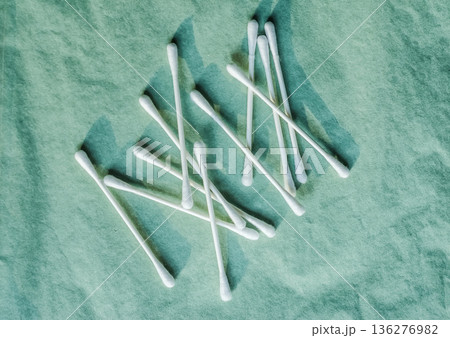 Scattered cotton swabs on a green textured background. Top view flat lay for hygiene and beauty concepts. Scattered cotton swabs on a green textured background. Top view flat lay for hygiene and beauty concepts. 136276982