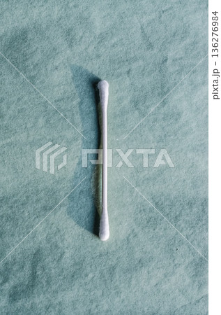 Minimalist flat lay of a single cotton swab on a textured green background. Hygiene and beauty tool with hard shadow. 136276984