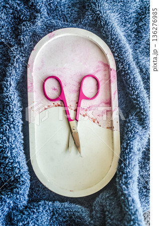 Manicure and self-care concept. Pink nail scissors on a decorative marble tray, set on a soft blue towel. Top view. Manicure and self-care concept. Pink nail scissors on a decorative marble tray, set on a soft blue towel. Top view. 136276985