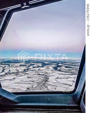 Pilots view from an airplane cockpit of a snowy winter landscape with a village and patchwork fields below. Pilots view from an airplane cockpit of a snowy winter landscape with a village and patchwork fields below. 136276998