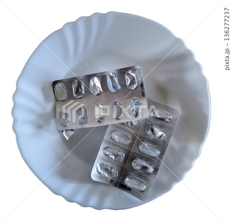 On a white plate, there are two empty packages of medicine. The packaging is metallic and shows that the capsules were removed. The setting is bright and clean. On a white plate, there are two empty packages of medicine. The packaging is metallic and shows that the capsules were removed. The setting is bright and clean. 136277237