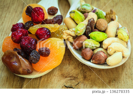 Varieties of dried fruits and nuts on wooden spoons. 136278335