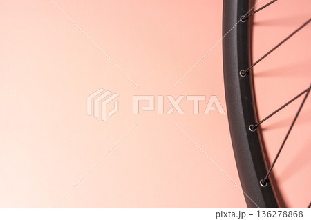 Close-up of a black bicycle rim with thin metal spokes radiating from the hub and casting shadows on a pink background. Close-up of a black bicycle rim with thin metal spokes radiating from the hub and casting shadows on a pink background. 136278868