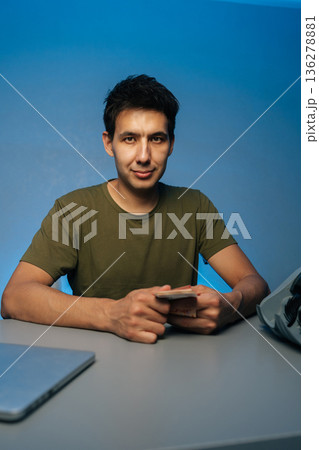 Vertical portrait of handsome cashier counting banknotes sitting at desk, using laptop and money counter machine, on isolated blue background, engaged in financial transactions and cash handling. Vertical portrait of handsome cashier counting banknotes sitting at desk, using laptop and money counter machine, on isolated blue background, engaged in financial transactions and cash handling. 136278881