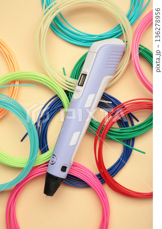 Children's 3D handle with plastic coils red, white, yellow, blue on beige background. Plastic PLA and ABS filament material for printing on a 3D pen 136278956