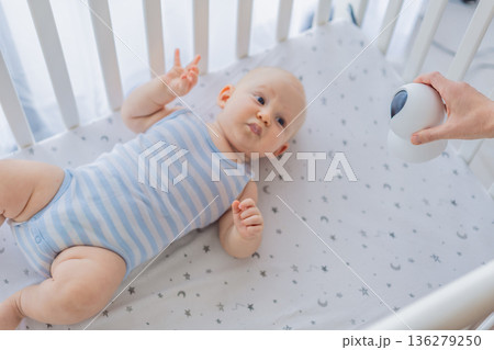 Baby monitor camera placed inside a crib where an infant is lying, ensuring safety and constant supervision. Modern parenting scene combining care and technology. Baby monitoring, security and smart 136279250
