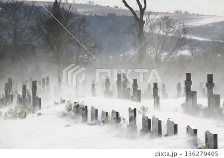 Snow-covered cemetery with rows of gravestones emerges through blowing winter mist, Snow-covered cemetery with rows of gravestones emerges through blowing winter mist, 136279405