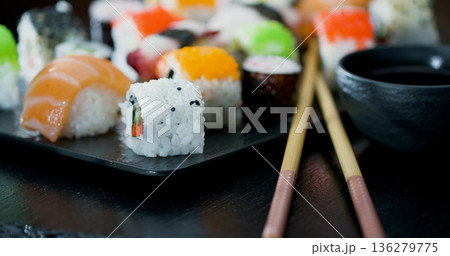 Sushi rolls are arranged on a black plate with chopsticks placed beside them at a dining table Sushi rolls are arranged on a black plate with chopsticks placed beside them at a dining table 136279775