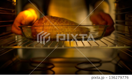 Cooking fish in a glass baking dish placed in the oven with hands reaching for it 136279776
