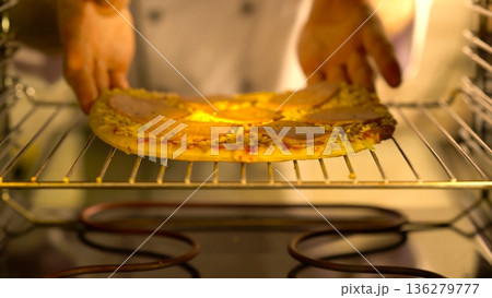 Hands take out a pizza from the oven in a kitchen during the afternoon 136279777