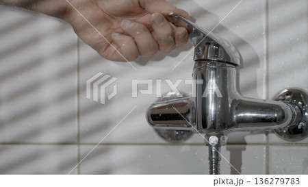 Water flow control from a faucet in a bathroom during the day with light creating shadows on the tiles 136279783