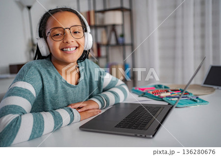 Happy schoolgirl learning online with laptop and headphones Happy schoolgirl learning online with laptop and headphones 136280676