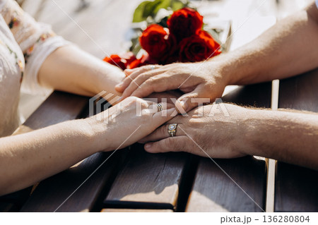 Wedding rings on intertwined hands with red roses, romantic closeup of couple, copy space Wedding rings on intertwined hands with red roses, romantic closeup of couple, copy space 136280804