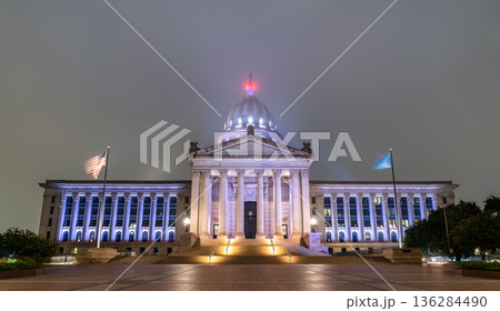 Night view of Oklahoma State Capitol in Oklahoma City. Neoclassical building features illuminated dome and columns amidst foggy atmosphere Night view of Oklahoma State Capitol in Oklahoma City. Neoclassical building features illuminated dome and columns amidst foggy atmosphere 136284490