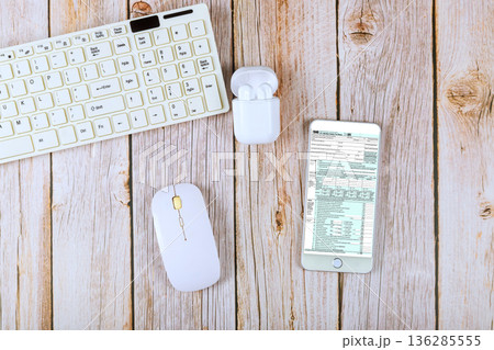Keyboard, mouse next to smartphone displaying 1040 tax form document, earbuds are open nearby on accounting office Keyboard, mouse next to smartphone displaying 1040 tax form document, earbuds are open nearby on accounting office 136285555
