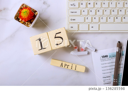 Number blocks display April 15 alongside earbuds 1040 tax forms on work desk. 136285598