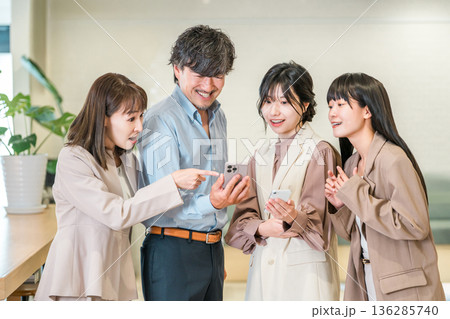 スマホを見ながら笑顔で会話するビジネスマンとビジネスウーマン 136285740