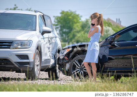 Sad female driver speaking on sellphone on street side calling for emergency service after car accident. Road safety and insurance concept 136286747
