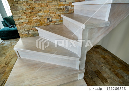 Stylish wooden contemporary staircase inside loft house interior. Modern hallway with decorative limestone brick walls and white oak stairs. 136286828