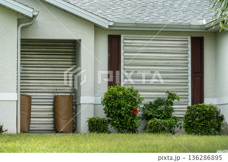 Boarded up windows with steel storm shutters for hurricane protection of residential house. Protective measures before natural disaster in Florida 136286895
