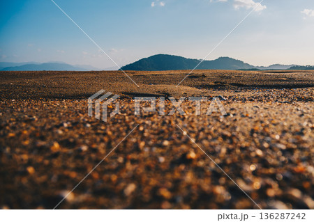 Low-Angle Sandy Beach with Distant Hills Under Clear Blue Sky Low-Angle Sandy Beach with Distant Hills Under Clear Blue Sky 136287242