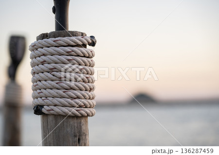 Rope Wrapped Around Wooden Post by Calm Sea at Sunset 136287459